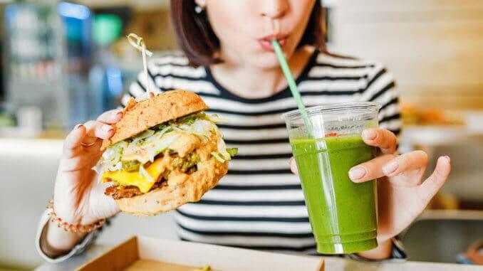 A young woman drinks green smoothies and eats a burger in a vegan fast food restaurant A young woman drinks green smoothies and eats a burger in a vegan fast food restaurant