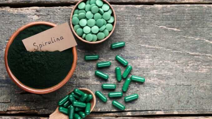 Spirulina powder and tablets on grey wooden table
