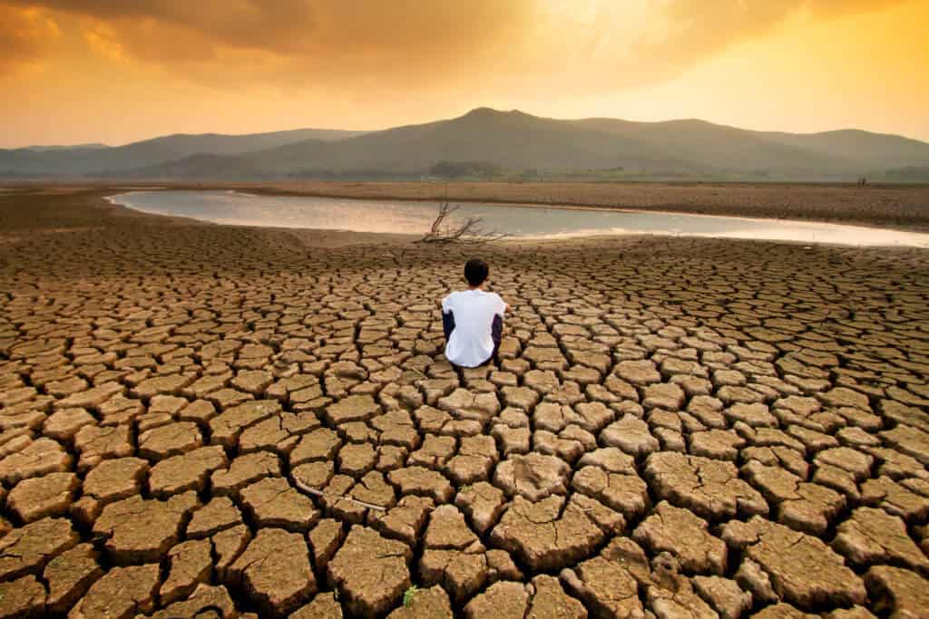 Climate change and global warming concept. Children sitting on drying lake with the sky turning orange by an pollution from industrial or city.