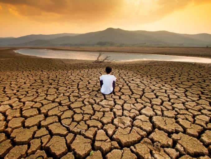 Climate change and global warming concept. Children sitting on drying lake with the sky turning orange by an pollution from industrial or city.