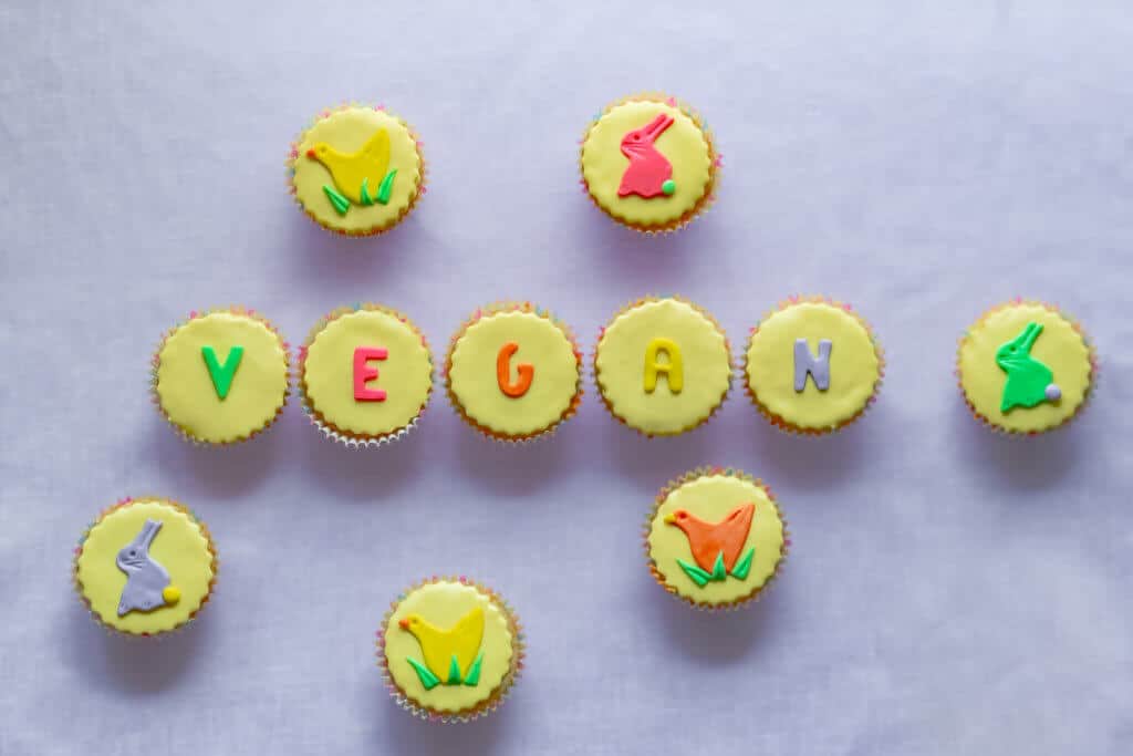 Pretty colorful yellow vegan Easter cupcakes with pastel icing shapes of Easter bunny rabbits and chicks and vegan word